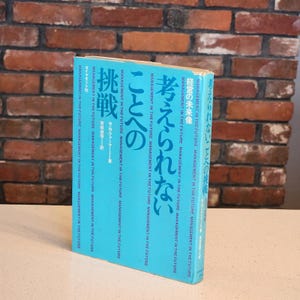 May include: A hardcover book with a light blue cover and Japanese text. The title includes the words "Management in the Future" and "Challenge". The book is standing on a white surface in front of a brick wall.