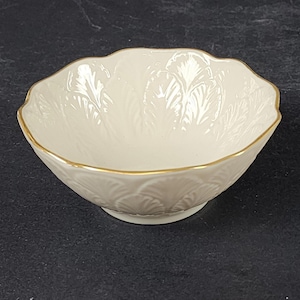 May include: Cream-coloured, scalloped-edge bowl with a gold rim. The bowl features a raised leaf pattern and a small, circular base. This decorative bowl is suitable for serving or display.