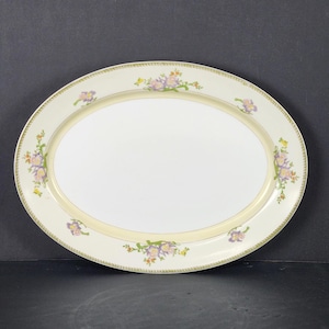 May include: Oval serving platter with a cream-colored border and a white center. The border features a delicate floral design in shades of purple, yellow, and green. A thin gold band accents the inner edge of the border.