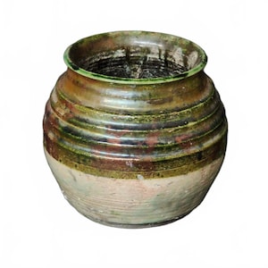 Op de afbeelding: Een ronde keramische pot met een brede opening. De pot heeft horizontale banden van kleuren, waaronder bruin, groen en crème. De rand is donkergroen. De pot heeft een rustieke, verouderde uitstraling, handgemaakt.