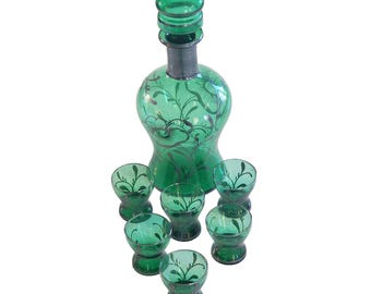 Puede incluir: Una jarra de vidrio verde con un tapón a juego y seis vasos pequeños. La jarra y los vasos presentan un diseño floral. El juego está hecho de vidrio verde con detalles plateados. La jarra mide aproximadamente 25 cm de altura.