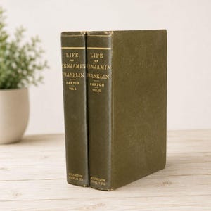 May include: Two olive green hardcover books titled Life of Benjamin Franklin by Parton, Volume I and Volume II. The spines feature gold lettering with the author name, title, volume number, and the publisher Houghton Mifflin Co. at the base.