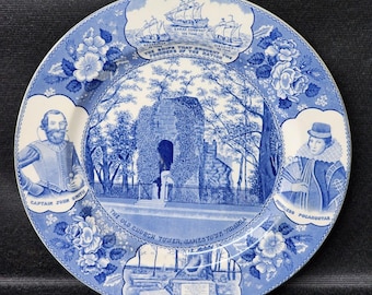 May include: A blue and white decorative plate with historical imagery. The plate depicts ships, Captain John Smith, Princess Pocahontas, and the Old Church Tower in Jamestown, Virginia. Floral designs and text frame the central scene.