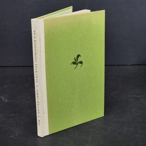 May include: A hardcover book titled "To a Blossoming Pear Tree" by James Wright. The book has a light green cover with a dark green floral design and white spine. The book is open, revealing the pages.