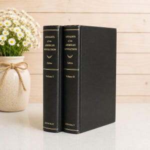 May include: Two black hardcover books titled Loyalists of the American Revolution by Sabine, Volume I and Volume II, featuring gold lettering and decorative lines on the spines, with the publisher name Kennikat printed at the bottom of each spine.