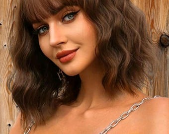 May include: A brown wavy bob wig with bangs. The wig is styled with loose waves and has a side part. The bangs are straight and fall just above the eyebrows.