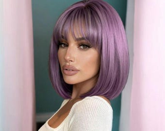 May include: A lavender bob wig with bangs. The wig has a smooth, sleek texture and a natural-looking hairline. The hair is styled in a chin-length bob with blunt bangs. The model is wearing a white long-sleeve shirt.