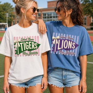 May include: A white t-shirt with a green pennant graphic reading TIGERS and a blue t-shirt with a purple pennant graphic reading LIONS. Both shirts feature a cream bow, vertical stripes, and the text School Name and Mrs. Jessica.