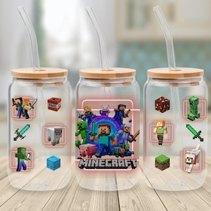 Könnte beinhalten: Drei transparente Glasbecher mit Bambusdeckeln und klaren Strohhalmen. Jeder Becher zeigt Minecraft-Charakterdesigns und das Minecraft-Logo. Die Becher stehen auf einer Holzoberfläche.
