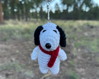 Op de afbeelding: Een handgemaakte gehaakte Snoopy sleutelhanger. De witte Snoopy heeft zwarte oren en een zwarte neus en draagt een rode sjaal. De sleutelhanger is bevestigd aan een zilveren metalen ring.