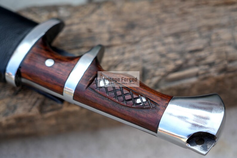 May include: Close-up of a wooden and metal knife handle with a checkered pattern and the text "Heritage Forged" on the side.