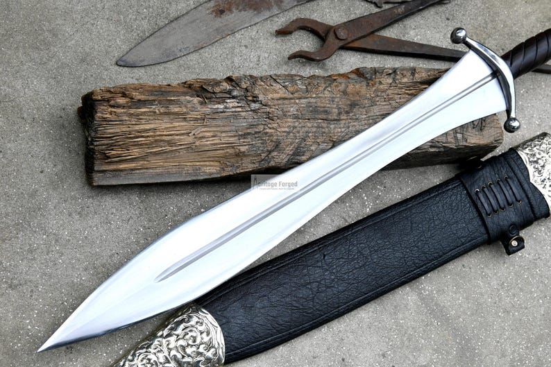 May include: A silver sword with a black leather scabbard and a wooden handle. The sword has a pointed tip and a double-edged blade.