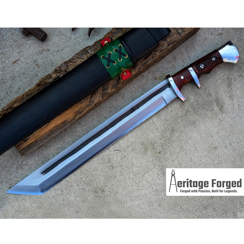May include: A silver and brown knife with a wooden handle and a black leather sheath. The knife has a long, sharp blade and a decorative design on the handle. The sheath has a green and red strap with the word "XXX" on it. The knife is on a wooden surface. The text "Heritage Forged" is on the bottom of the image. "Forged with Passion, Built for Legends."