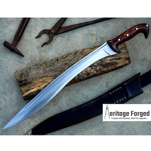 May include: A curved, silver-colored sword with a wooden handle and a brown leather sheath. The sword is resting on a piece of wood and the sheath is lying on a gray surface. The text "Heritage Forged" is visible in the lower right corner of the image.  Forged with Passion, Built for Legends.