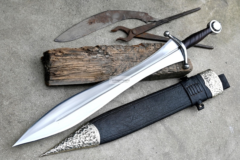 May include: A silver sword with a black leather scabbard and a silver pommel. The sword has a long, straight blade and a crossguard. The scabbard has a silver tip and a silver band around the middle.