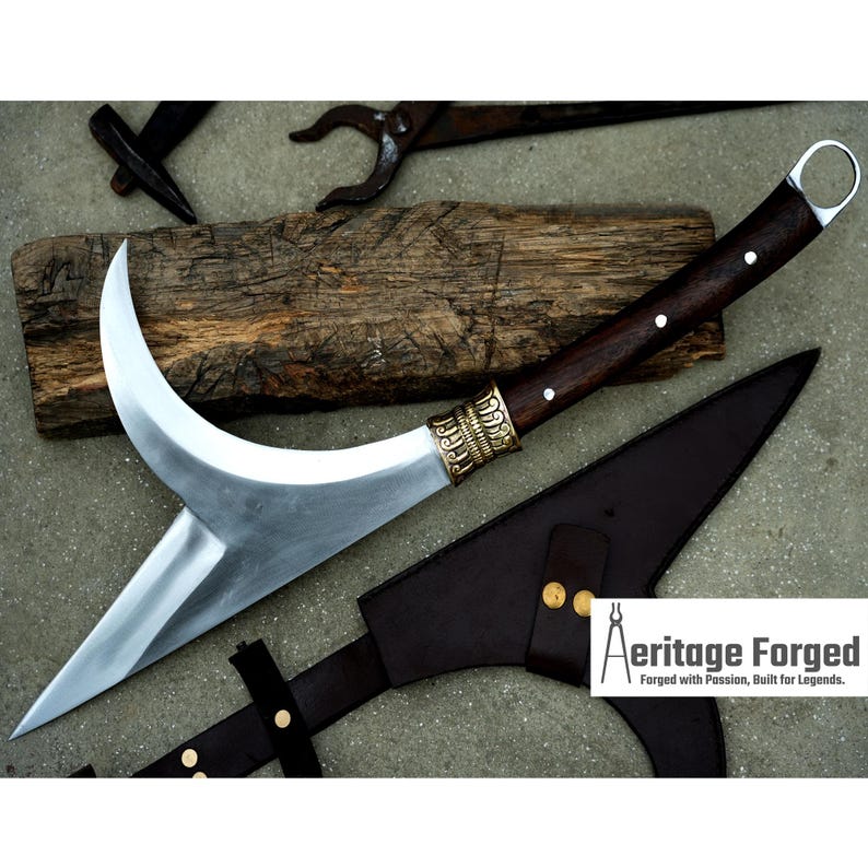 May include: A curved, silver-colored blade with a brown wooden handle and brass accents. The blade is attached to a brown leather sheath with brass accents. The text "Heritage Forged, Forged with Passion, Built for Legends." is visible in the lower right corner of the image.