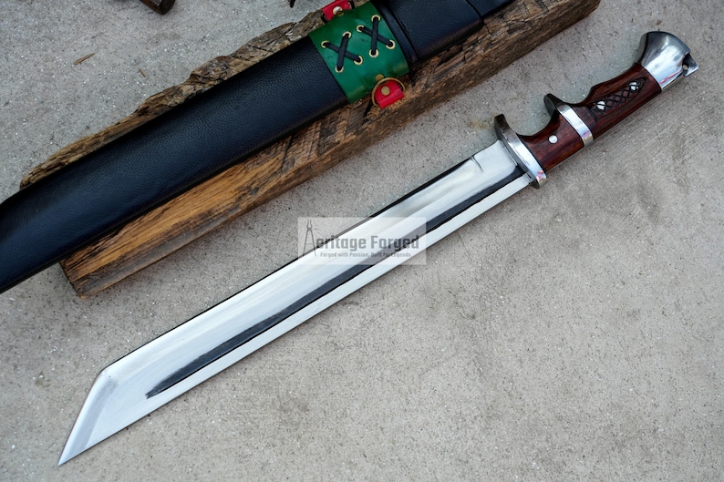 May include: A silver and brown handled knife with a long, sharp blade. The knife is resting on a wooden surface with a black leather sheath.