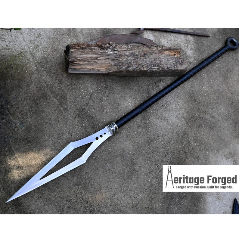 Puede incluir: Una lanza negra y plateada con una hoja en forma de diamante y un mango negro. La lanza mide aproximadamente 1,5 metros de largo y tiene una pieza de metal decorativa cerca de la hoja. La lanza est&aacute; sobre una superficie de hormig&oacute;n. El texto "Heritage Forged" es visible en la esquina inferior derecha de la imagen. "Forjado con pasi&oacute;n, construido para leyendas."