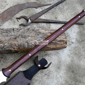 May include: A brown wooden handled spear with a silver metal tip and a leather sheath. The spear is resting on a wooden log.