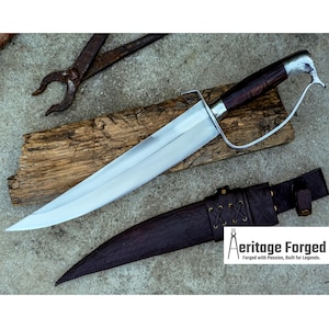 May include: A large, polished steel blade knife with a dark wooden handle and a curved guard. The knife rests on a wooden plank, with a leather sheath below. The text "Aeritage Forged" is visible.