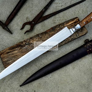 May include: A long, silver blade with a wooden handle and a leather sheath. The blade is sharp and pointed, and the handle is decorated with a simple design. The sheath is brown leather with a strap and buckle.
