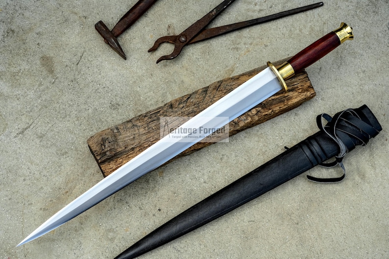 May include: A handmade dagger with a polished silver blade, a dark wood handle, and a brass guard. The dagger rests on a wooden plank, accompanied by a black leather sheath. Blacksmith tools are in the background.