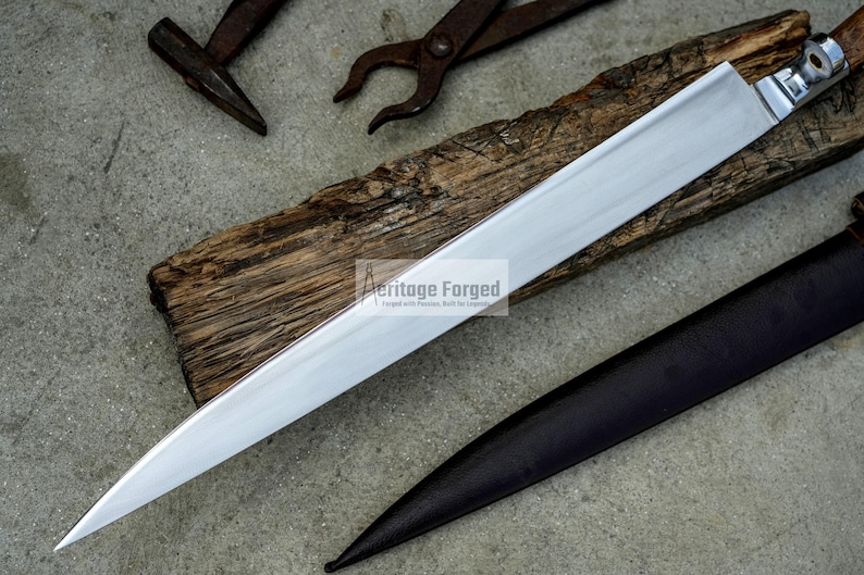 May include: A long, silver blade with a wooden handle and a leather sheath. The blade is sharp and pointed, and the handle is decorated with a metal design. The sheath is brown and has a flap that closes with a buckle.