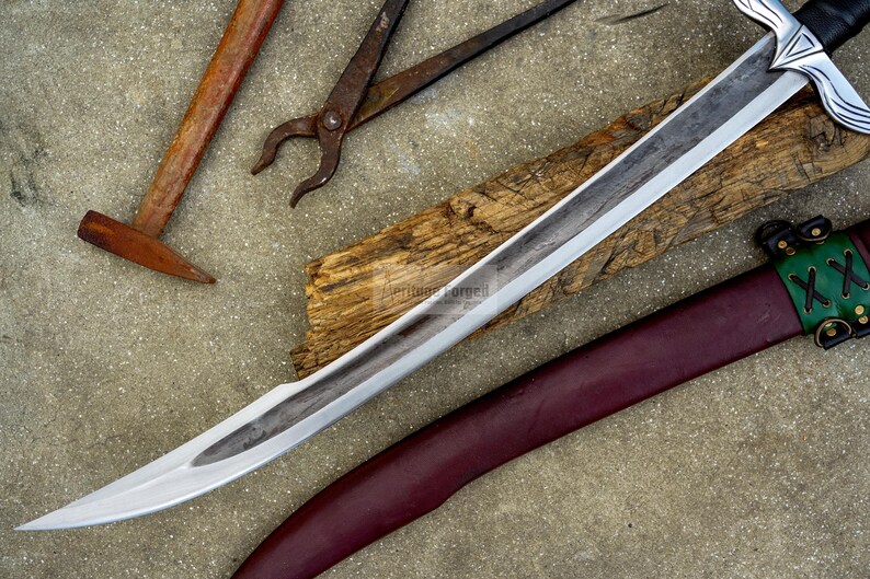 May include: A medieval-style sword with a silver blade and a decorative hilt, resting on a wooden plank. A burgundy leather sheath with green accents is visible. Also, a hammer and pliers are in the image.