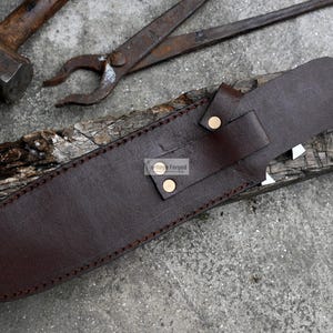 Puede incluir: Una funda de cuero marr&oacute;n con un borde cosido y dos remaches de lat&oacute;n. La funda est&aacute; dise&ntilde;ada para sostener un cuchillo u otro objeto afilado.
