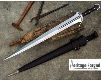May include: A silver and black sword with a curved blade, resting on a piece of wood. A black sheath and tools are also present. The sword has a black handle and a silver guard. The text "Aeritage Forged" is visible.