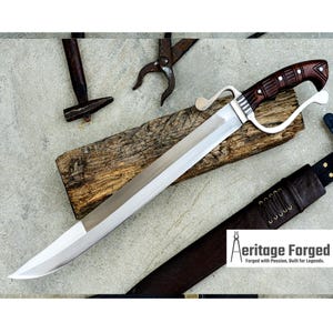 May include: A large, polished steel sword with a wooden handle and a curved guard. The handle is dark brown with decorative carvings. The sword rests on a wooden plank, with a leather sheath visible. The image includes blacksmith tools.