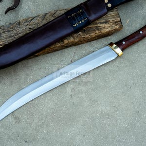 May include: A curved, silver-colored knife with a wooden handle and brass accents. The knife is resting on a wooden surface and has a leather sheath.