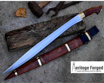 May include: A long, silver blade with a wooden handle and a brown leather sheath. The blade is sharp and pointed, and the handle is decorated with brass accents. The sheath has a brass accent at the top and a black leather strap.