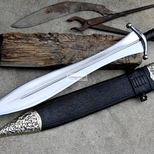 May include: A silver sword with a black leather scabbard and a silver pommel. The sword has a long, straight blade and a crossguard. The scabbard has a silver tip and a silver band around the middle.