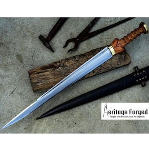 May include: A silver sword with a wooden handle and brass accents. The sword is lying on a wooden surface with a black leather scabbard. The image also includes a hammer and pliers.