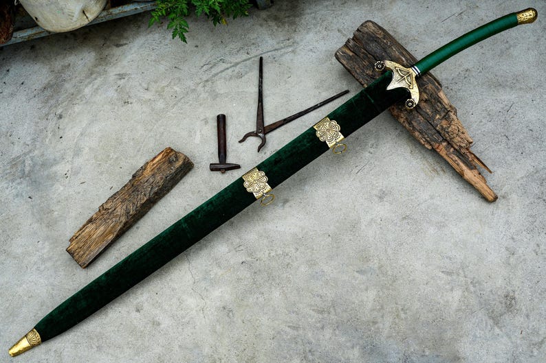 May include: A decorative sword with a green velvet scabbard and handle, featuring gold-colored accents. The sword rests on a wooden surface, with additional small metal tools nearby. The blade is not visible.