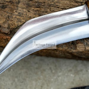 May include: A curved, silver-coloured knife with a wooden handle. The knife is resting on a piece of wood.
