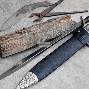 May include: A silver and black sword with a leather scabbard. The sword has a decorative handle and a sharp blade. The scabbard has a silver design.
