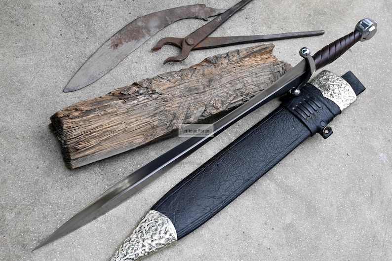 May include: A silver and black sword with a leather scabbard. The sword has a decorative handle and a sharp blade. The scabbard has a silver design.