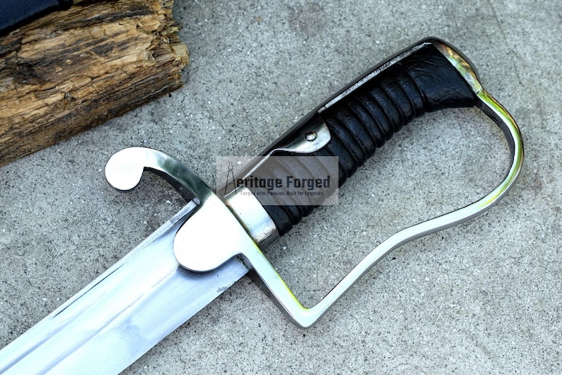 May include: Close-up of a saber with a silver blade and guard, and a black leather-wrapped handle. The text "Heritage Forged" is visible on the blade. The saber is on a gray surface.