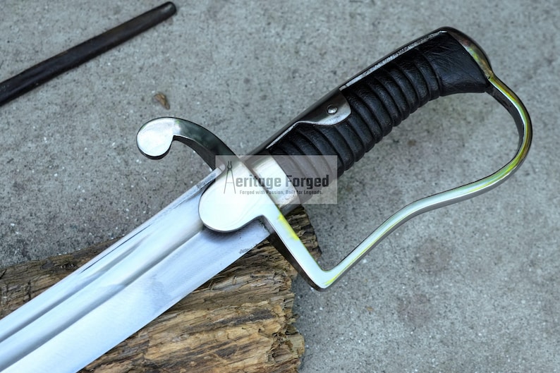 May include: A close-up of a saber with a silver blade and a black, textured handle. The hilt has a curved guard and a decorative pommel. The text "Heritage Forged" is visible on the blade. The saber rests on a wooden surface.