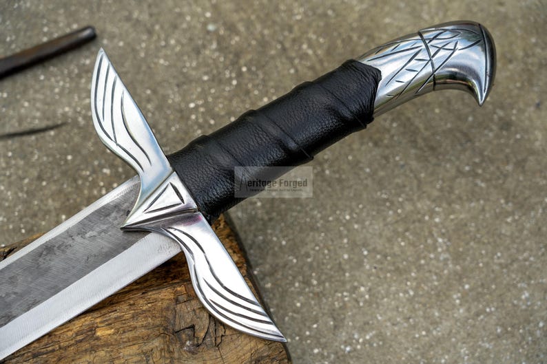May include: Close-up of a silver sword with a black leather-wrapped handle. The blade is silver and the handle has intricate designs. The sword rests on a wooden surface, showcasing its detailed craftsmanship.