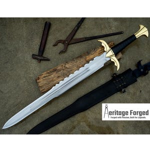 May include: A silver sword with a black leather handle and a gold-colored pommel. The sword has a serrated edge and is resting on a black leather scabbard. The sword is on a wooden surface with a hammer and pliers in the background. The image includes the text "Heritage Forged, Forged with Passion, Built for Legends."
