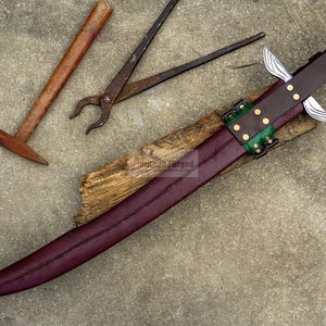 May include: A handcrafted sword with a burgundy blade and a brown leather sheath, accented with green and gold details. A hammer and pliers are visible in the background, suggesting a blacksmithing theme.