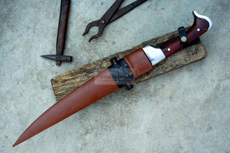 May include: A brown leather-sheathed knife with a silver blade and a wooden handle. The knife is on a piece of wood with the text "Heritage Forged" on the sheath.