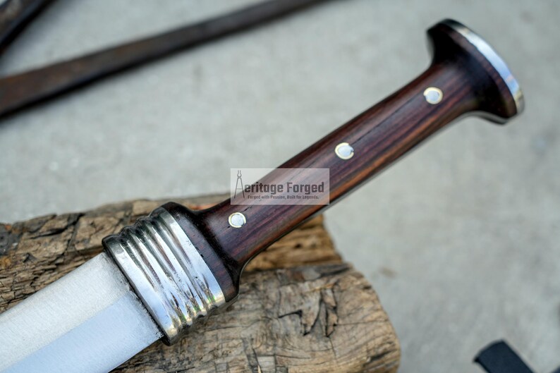 May include: A close-up of a knife with a dark wood handle and a silver blade. The handle has a decorative silver band and two silver dots. The text "Heritage Forged" is visible on the handle.