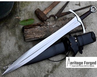 May include: A silver sword with a black leather scabbard and a wooden handle. The sword is lying on a gray surface with a hammer, pliers, and a piece of wood in the background. The text "Heritage Forged" is visible in the lower right corner of the image.  Forged with Passion, Built for Legends.