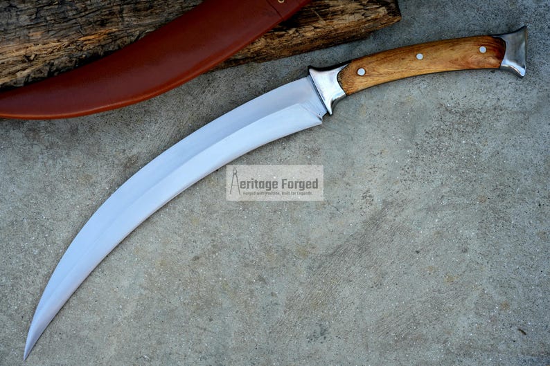 May include: A curved, silver-colored knife with a wooden handle. The handle has a brown wood grain and two silver rivets. The knife is on a gray concrete surface. The text "Heritage Forged" is visible in the image.