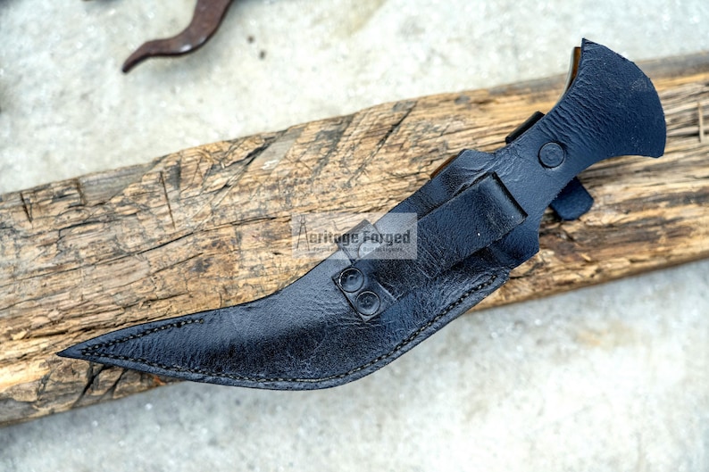 May include: Black leather knife sheath with a curved blade and a metal tip. The sheath has a decorative stitching detail and a metal button.