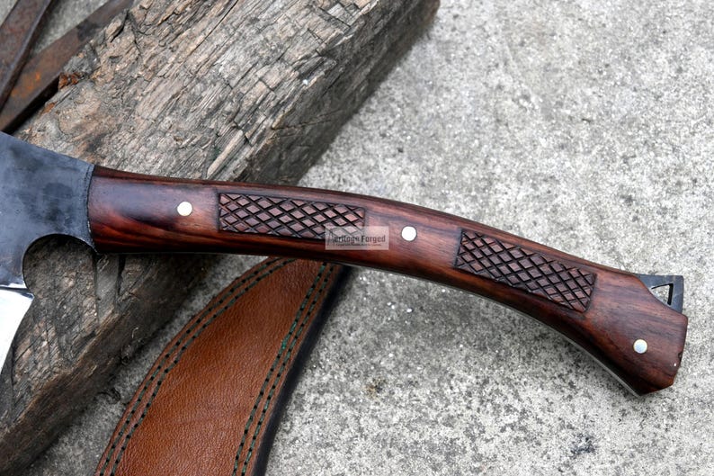 May include: Close-up of a handcrafted knife with a dark wooden handle. The handle features a carved diamond pattern and is secured with silver rivets. A leather sheath is partially visible.